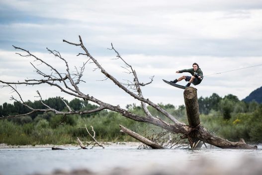 Wakeboarder springt über Baumstamm im Wasser